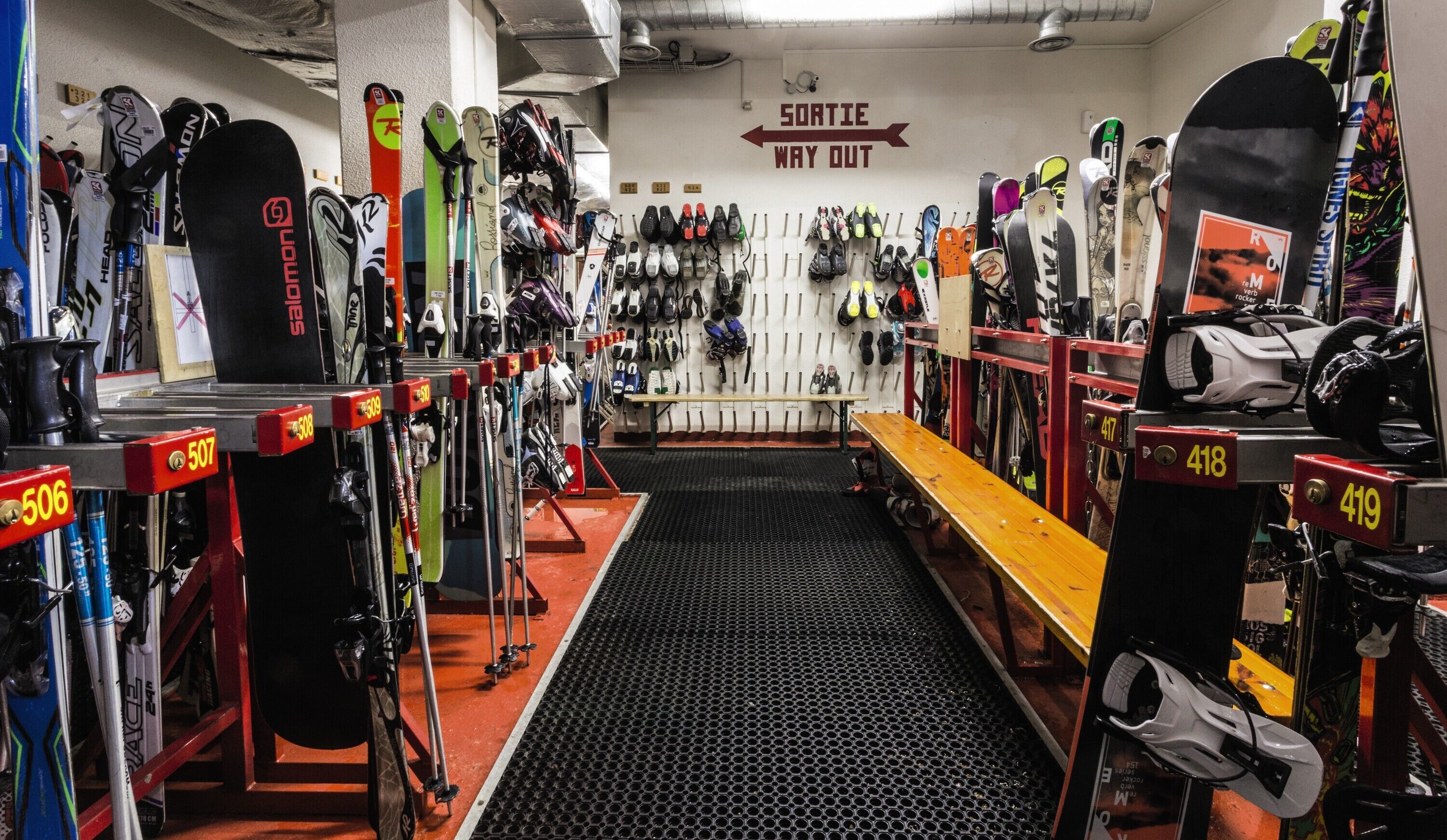 A ski rental shop with rows of skis and snowboards, a bench, and a sign indicating the exit.