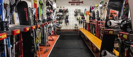 A ski rental shop with rows of skis and snowboards, a bench, and a sign indicating the exit.