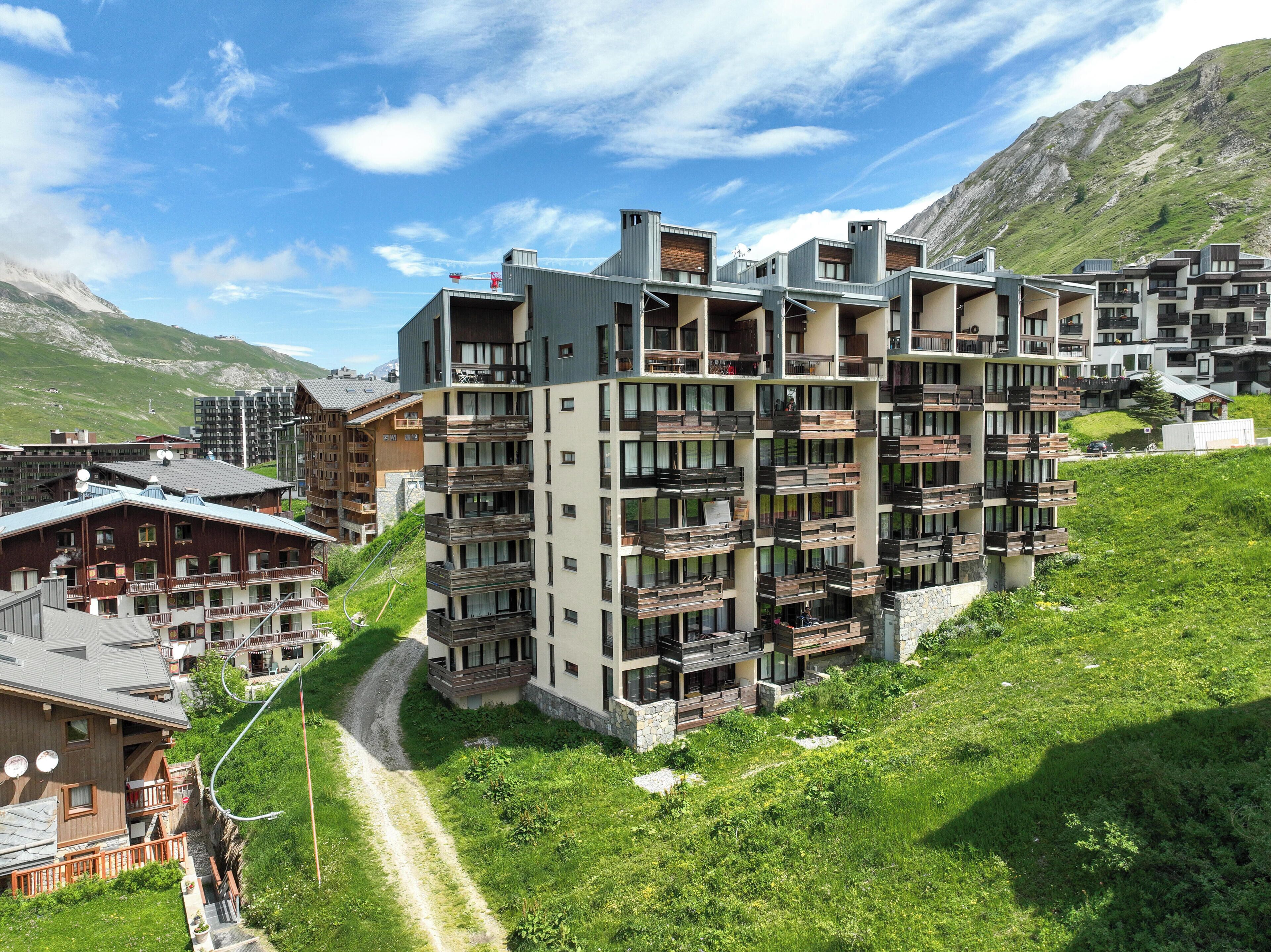 Un hôtel à plusieurs étages doté de balcons, une piste de ski et un paysage montagneux en arrière-plan.