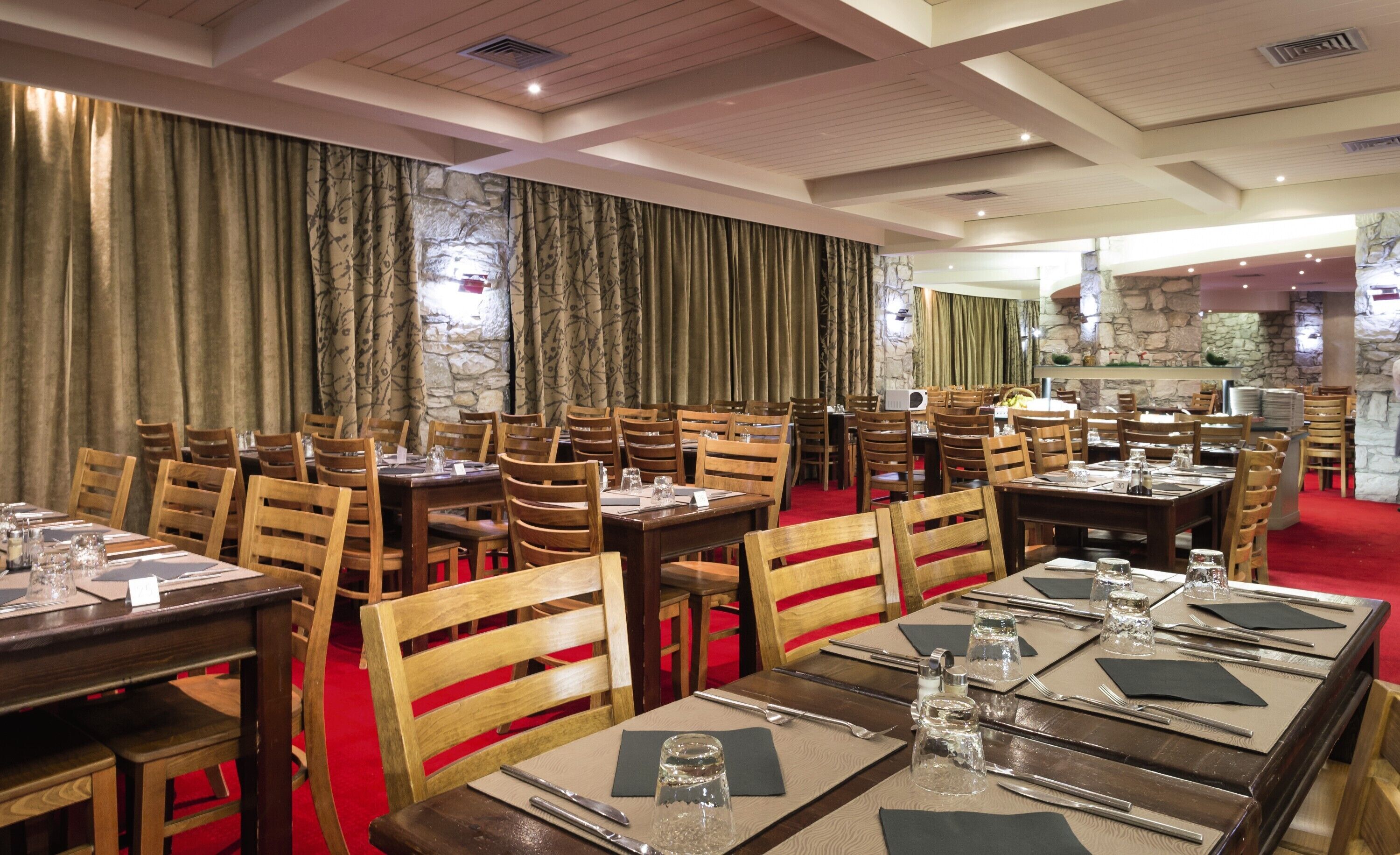 A restaurant with multiple wooden tables and chairs, stone walls, and red carpeting.