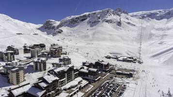 Une ville de montagne enneigée, avec des bâtiments modernes, une piste de ski et un ciel bleu dégagé.