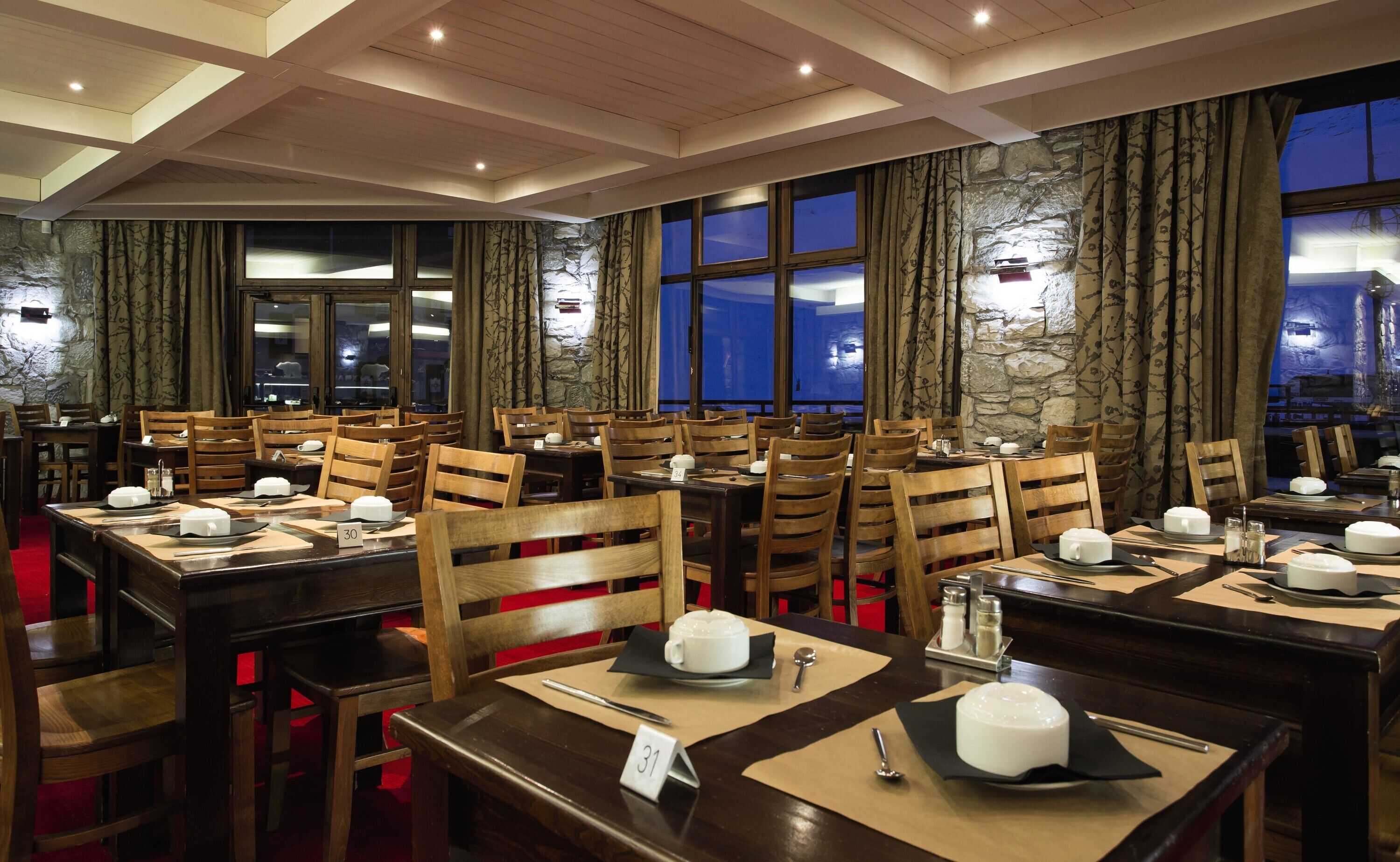 A restaurant with multiple tables and chairs, each set with plates, cutlery, and a teapot.