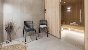Un moderno spa con dos sillones negros, un banco de madera y un ventanal que da a una zona de sauna.