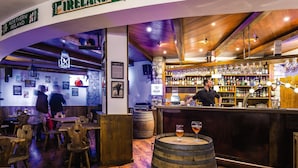 Una zona de bar con mobiliario de madera, un barman y una variedad de botellas y vasos en estanterías.