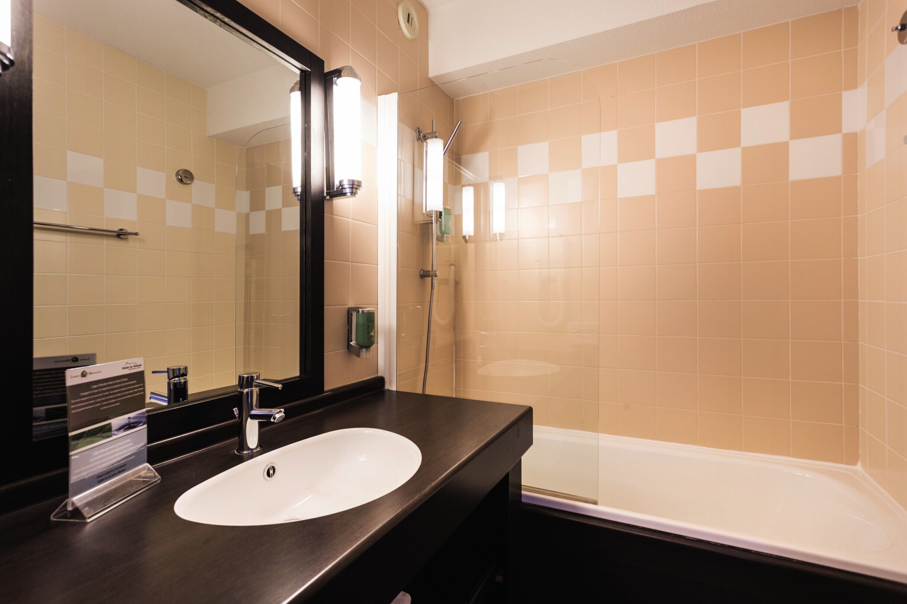 A bathroom with a white sink, dark countertop, and a large mirror.
