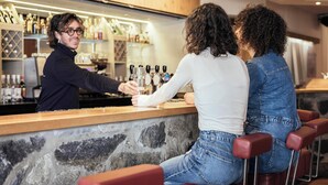 Zona de bar con pared de piedra, estantes de madera con botellas y taburetes rojos.