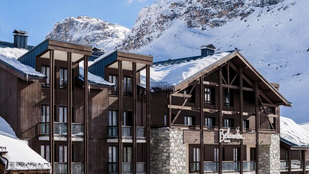 Un edificio de estilo chalet de madera con varios balcones y ventanas amplias, con una imponente montaña nevada al fondo.