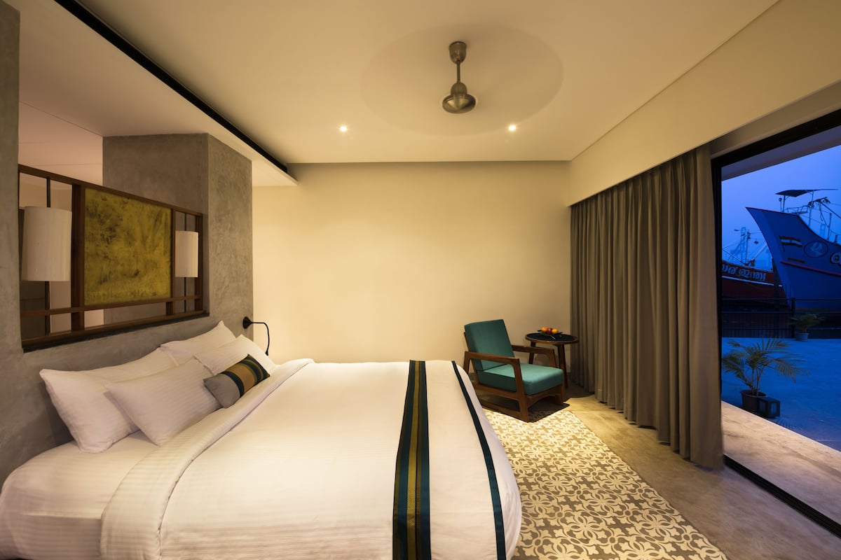 A modern hotel room with a large bed, a desk, a chair, and a view of the outside.
