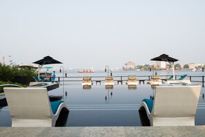 Una piscina a sfioro con lettini e ombrelloni, affacciata su uno specchio d'acqua con barche ed edifici in lontananza.