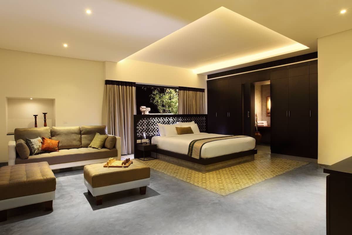 A modern hotel room with a sofa, a bed, a nightstand, and a desk.