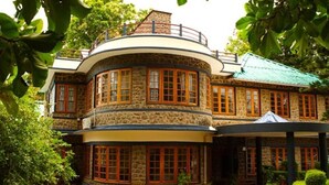 A stone building with multiple windows and a curved roof, surrounded by greenery.