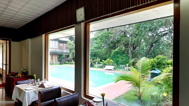 A dining area with a view of a swimming pool and lush greenery.