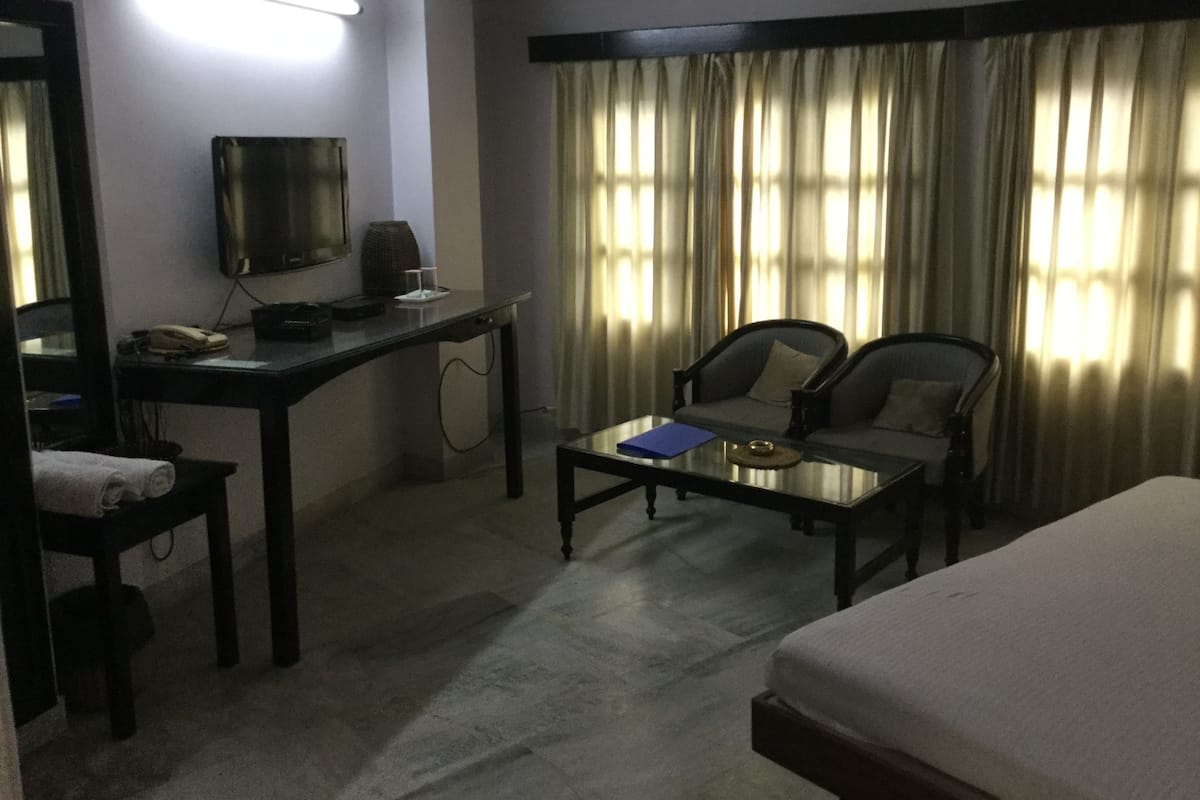 A hotel room with a bed, a desk with a telephone, a chair, a coffee table, and a television.