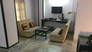 A living room with a sofa set, a coffee table, a desk with a computer, and a flat-screen TV mounted on the wall. - Hotel Mewar Inn (Udaipur)