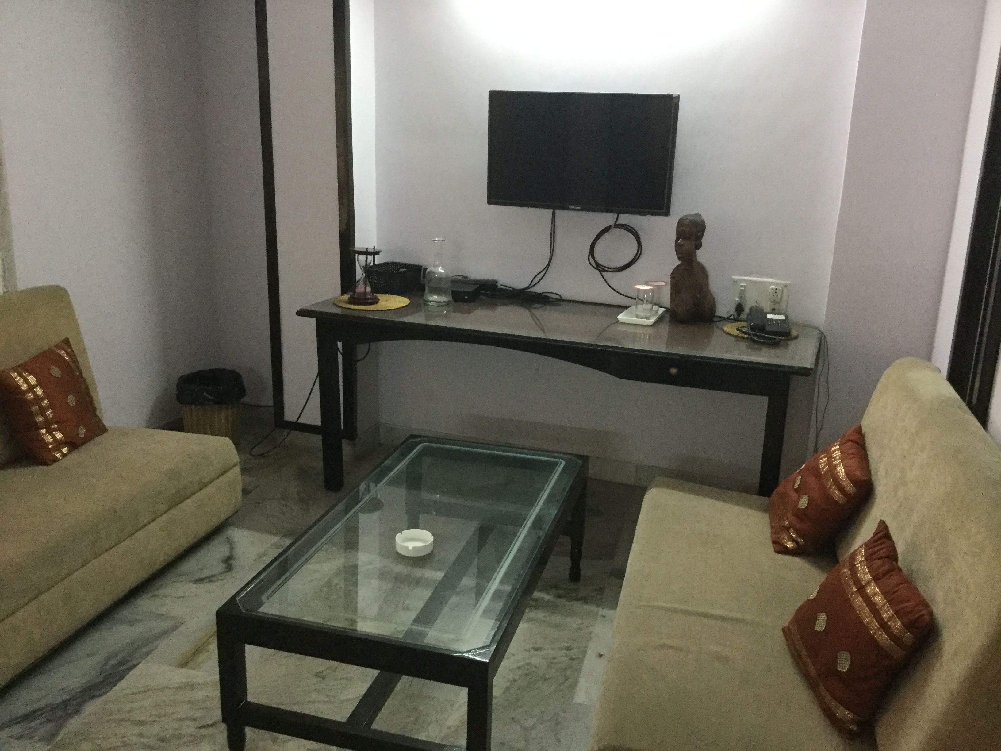 A living room with a sofa, a glass coffee table, a desk with a flat-screen TV, and a small statue.