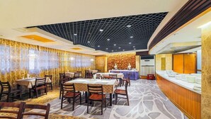 Zona de dinar d'hotel amb taules i cadires, un mostrador de menjar a gran bufet i una catifa amb dibuixos.