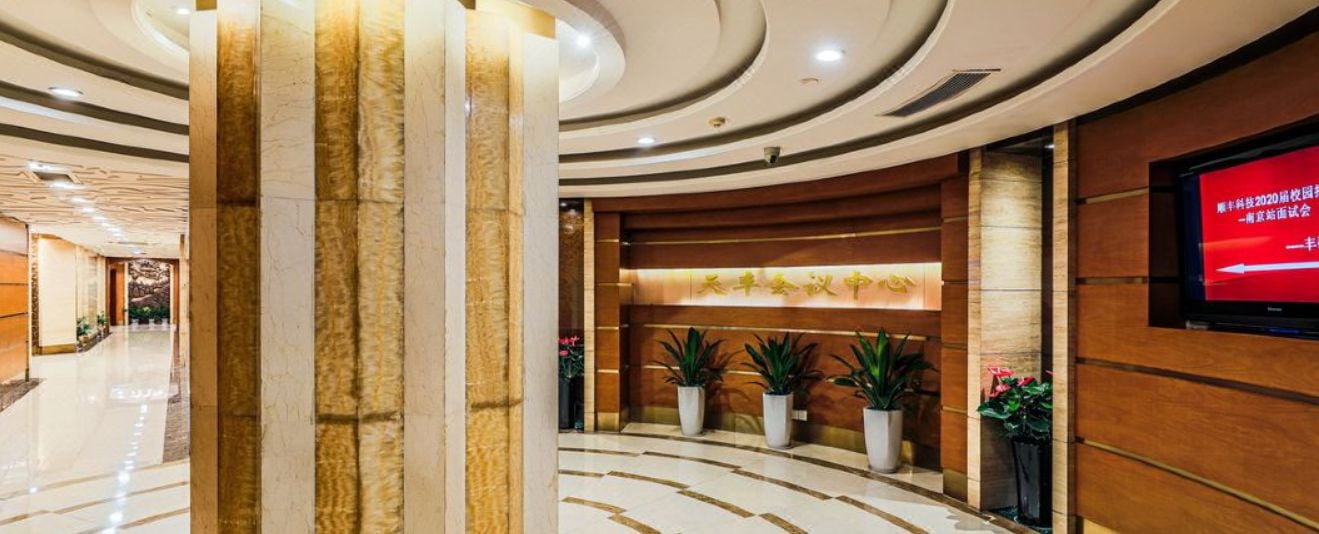 A hotel lobby with a reception desk, potted plants, and a television screen.