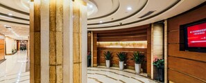 A hotel lobby with a reception desk, potted plants, and a television screen. - Tianfeng (Nanjing)