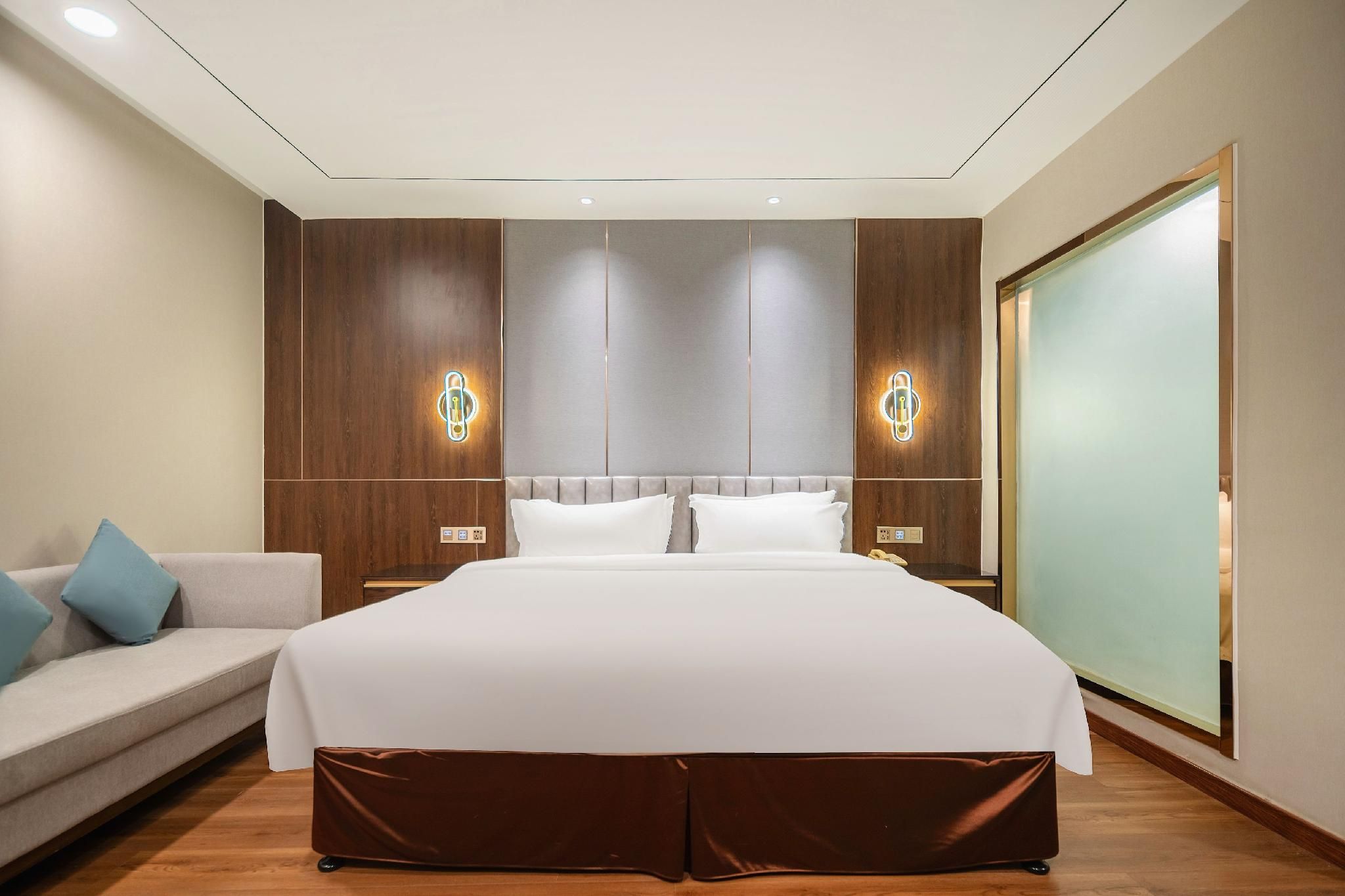 A modern hotel room with a large bed, a sofa, and a sliding door.