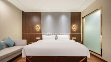 A modern hotel room with a large bed, a sofa, and a sliding door.