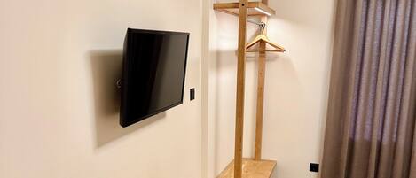 A hotel room with a wooden bench, a mounted TV, an air conditioning unit, and a bed.