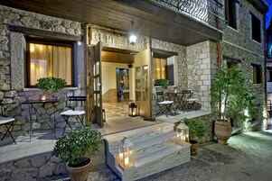 Un edificio de piedra con balcón de madera, asientos al aire libre y entrada iluminada.