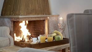 Een gezellige kamer met een open haard, een dienblad met fruit en drankjes, en een stoel.