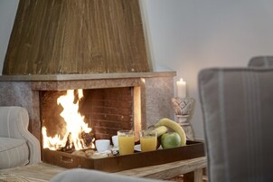 A cozy room with a fireplace, a tray with fruits and drinks, and a chair.