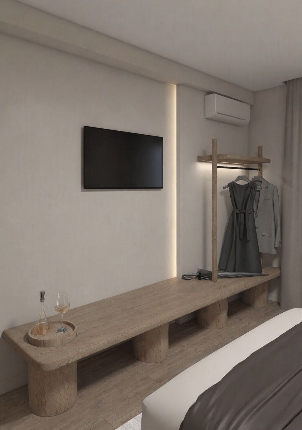 A modern hotel room with a wooden bench, a flat-screen TV mounted on the wall, a coat rack with clothes, and a bedside table with a wine glass and bottle.