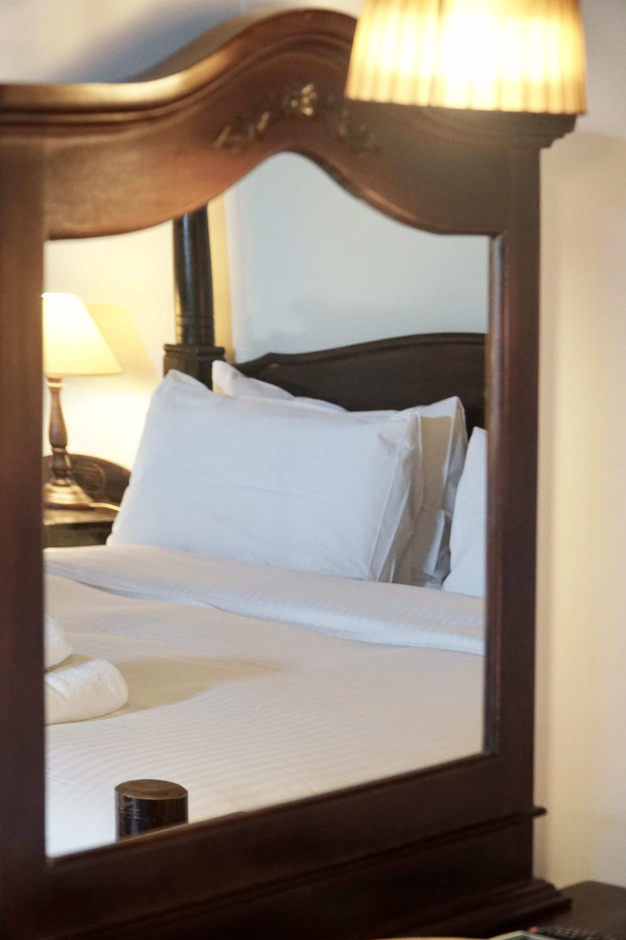 Una cama bien hecha con sábanas blancas y almohadas, cabecera de madera y una lámpara de noche.