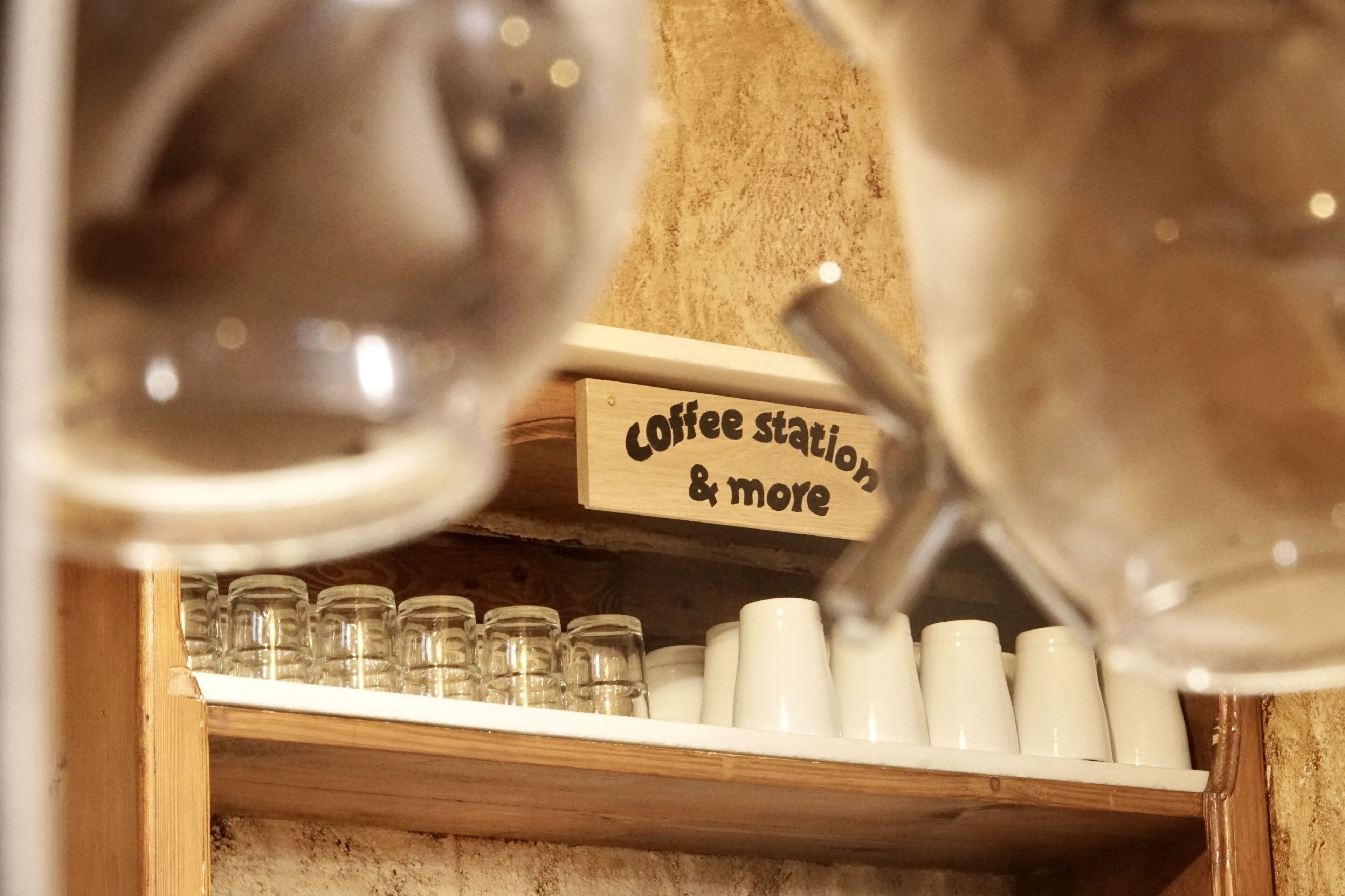 Ein Kaffee-Bereich mit einem Schild, auf dem ‚Coffee station & more‘ steht, und einem Regal mit Tassen und Gläsern.
