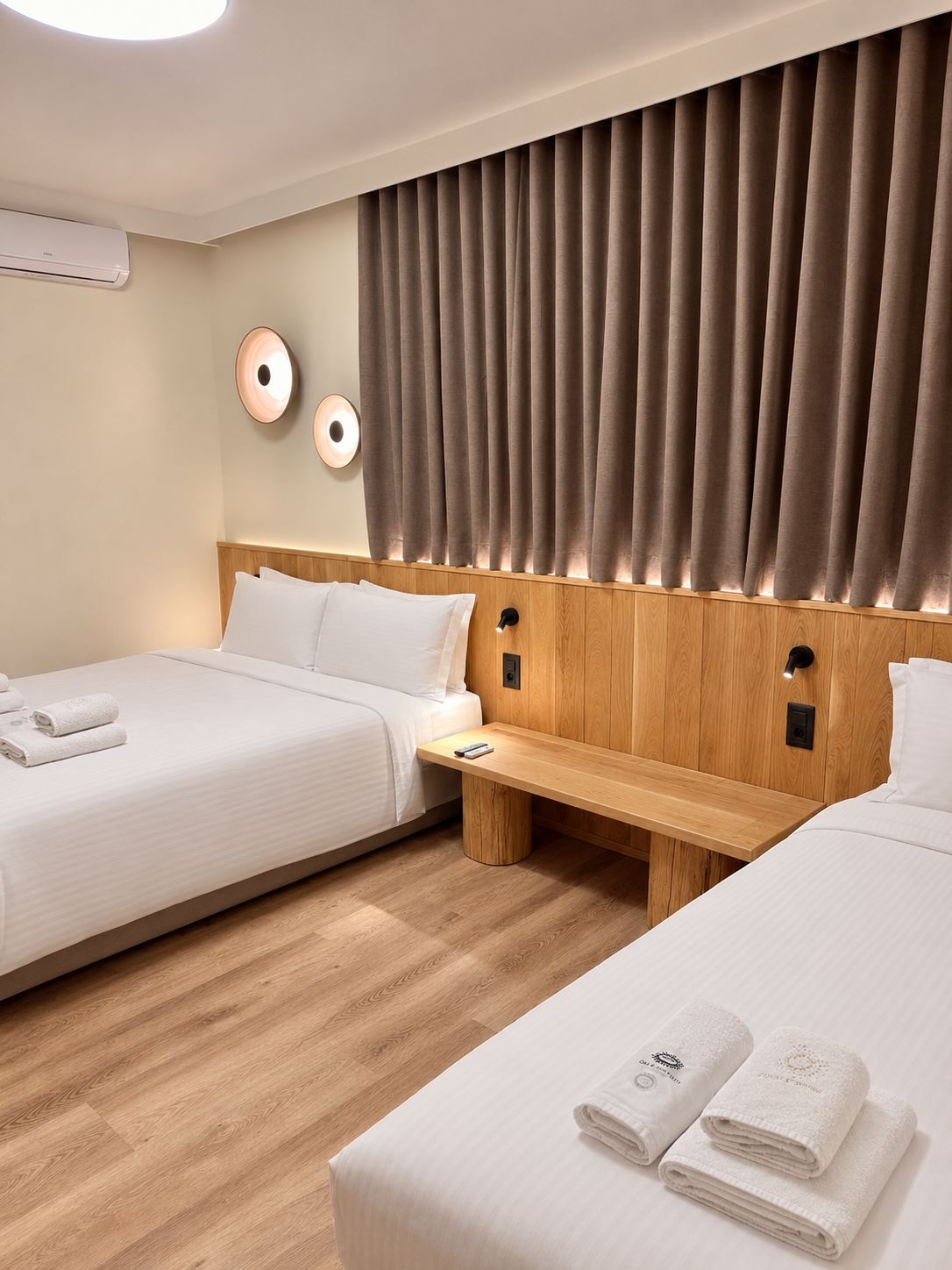 A hotel room with two beds, a wooden headboard, a bedside table, and a wall-mounted air conditioner.