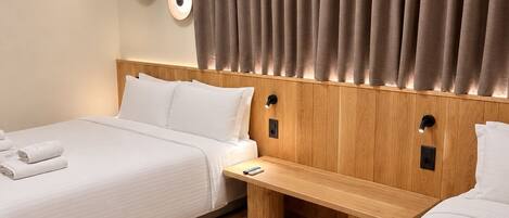A hotel room with two beds, a wooden headboard, a bedside table, and a wall-mounted air conditioner.