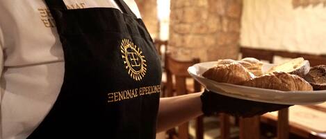A person in a black apron with a logo, holding a plate with pastries.