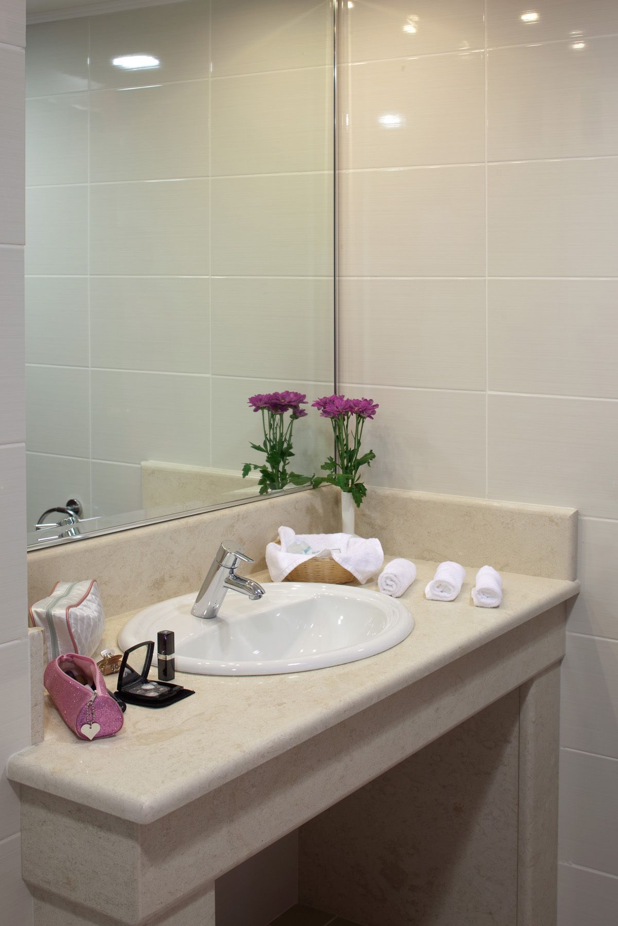 Un bagno con un lavandino bianco, uno specchio e un vaso con fiori viola.