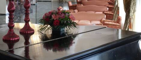 A grand piano in a spacious room with elegant chandeliers, plush seating, and a large window offering a view.