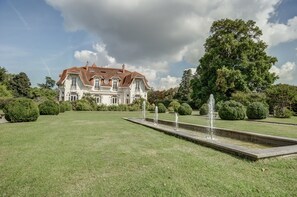 Una casa grande e histórica con un césped bien cuidado y una fuente central.