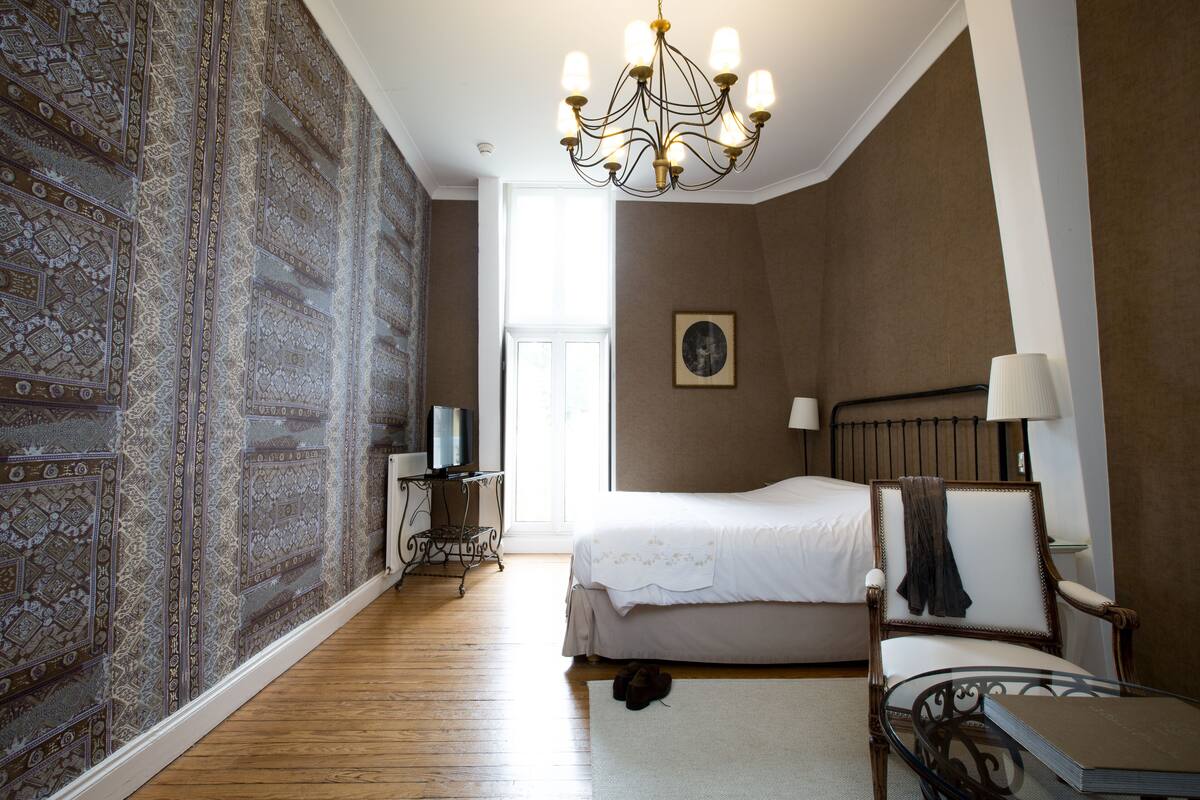 Een slaapkamer met een groot bed, een stoel, een tafel, een televisie en een behang met patroon.