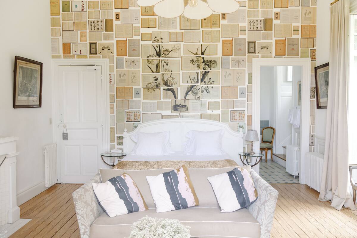 Een slaapkamer met een groot bed, een bank met decoratieve kussens, een muur versierd met ingelijste foto's, en een witte deur.
