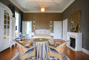Un dormitorio con una cama, una mesa redonda, sillas de mimbre, una chimenea y un espejo grande.