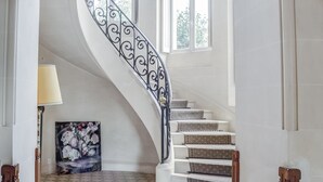 Un magnifique escalier avec une rampe en fer forgé, menant à un palier doté d’une grande fenêtre.