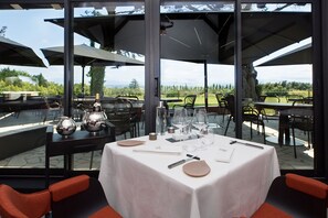 An outdoor dining area with a table set for two, surrounded by chairs, and a view of the landscape.
