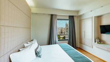 A hotel room with a bed, a TV, a window with curtains, and a view of buildings.