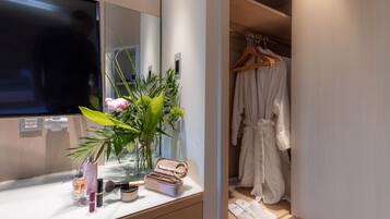 Une salle de bain avec un meuble-lavabo, un miroir et une plante. Une robe est suspendue à un porte-manteau et une paire de chaussons est posée sur le sol.