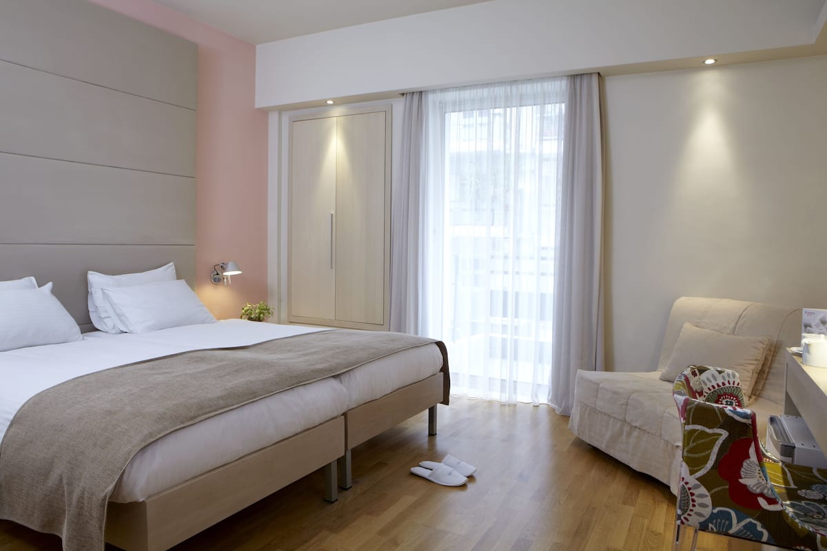 Una habitación de hotel moderna con una cama grande, un sofá pequeño, un escritorio con lámpara y una ventana con cortinas.