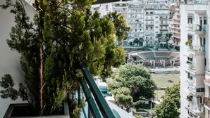 Vista desde un balcón sobre una zona urbana densamente poblada con edificios de varios pisos, un amplio espacio abierto con una estructura circular y un árbol en primer plano.