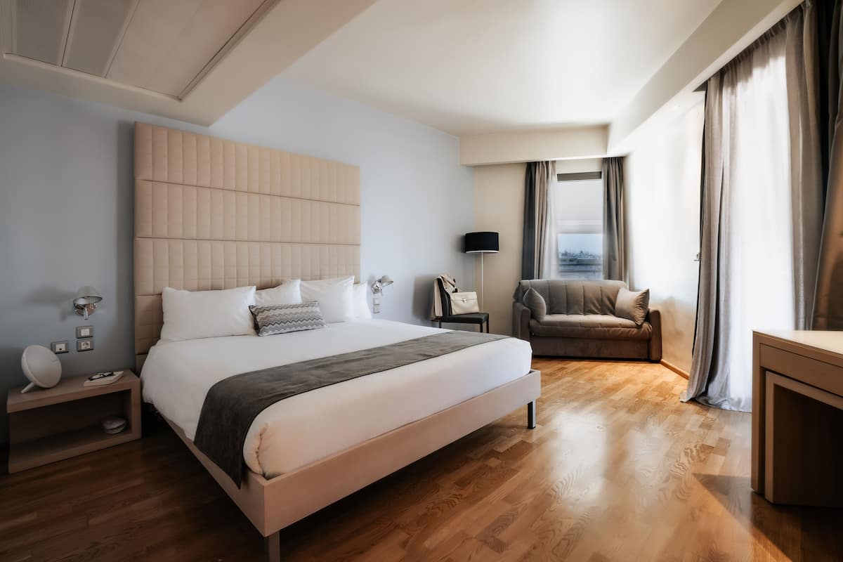 Habitación de hotel moderna con una cama grande, un sofá, un escritorio y vistas a la ciudad.