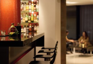 Un espace bar avec un comptoir, quelques chaises et un arrière-plan flou où l’on aperçoit des personnes.