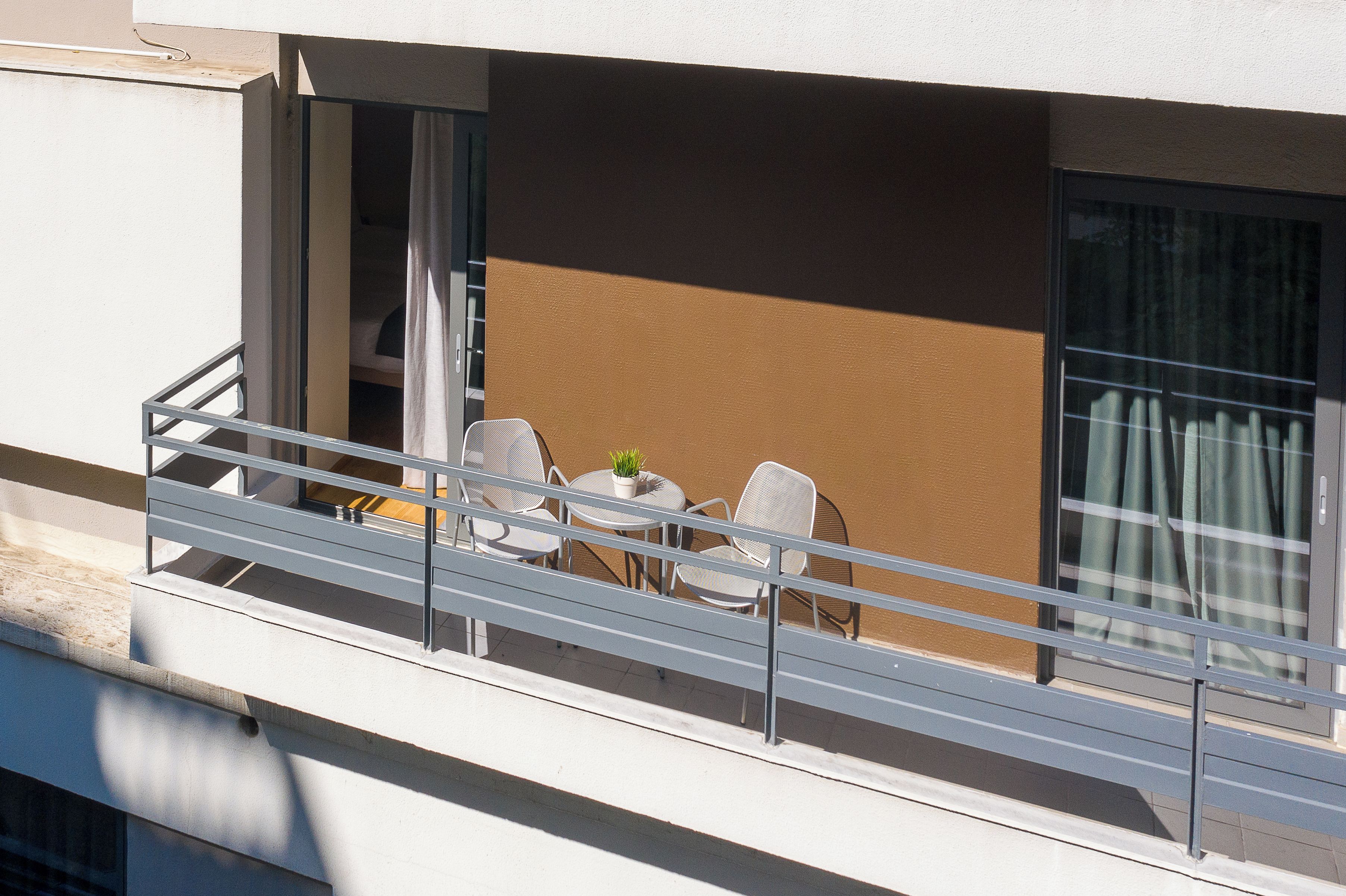 Un balcón con mesa y sillas, una planta en maceta y vistas de un edificio.
