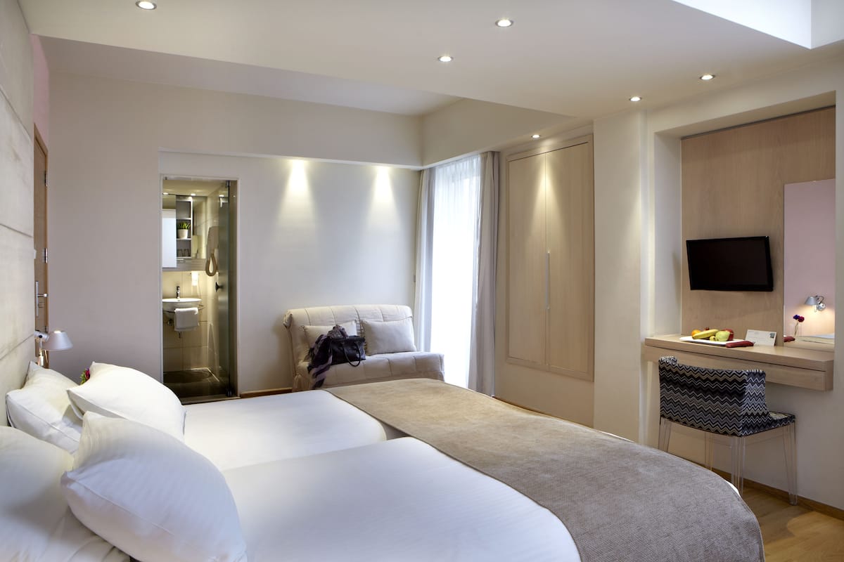 Una habitación de hotel moderna con una cama grande, un escritorio con silla, un televisor y un baño visible a través de una puerta abierta.